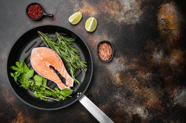 Taze çiğ somon bifteği seti, dökme demir kızartma tavasında, eski koyu kırsal masa zemininde, üst görünüm düz yerde, metin için kopya alanı ile