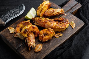 Mango soslu kızarmış kaplan karidesleri ve ahşap tahtada, siyah ahşap masa arkasında gevrek sarımsak seti.