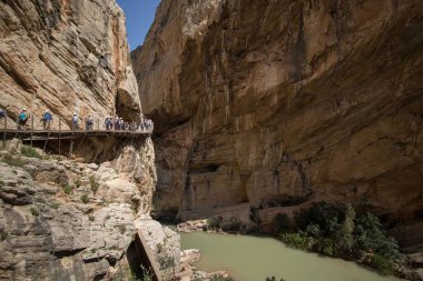 Güneşli bir günde Caminito del Ray 'de yürüyen turistler, kanyonlar arasında nehir.