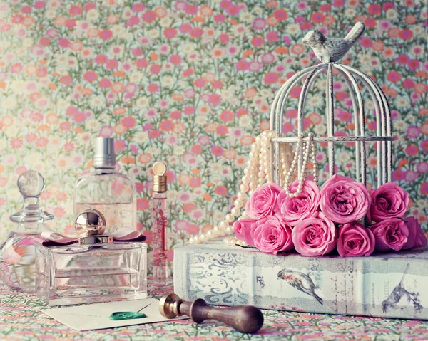 Birdcage with peonies on book and perfumes — Stock Photo, Image