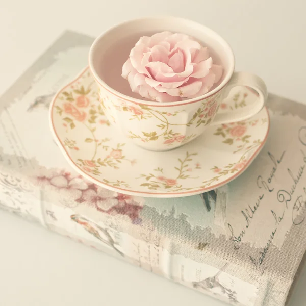 Роза в чашке чая на книге — стоковое фото