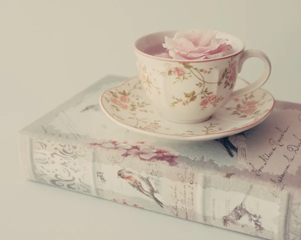 Rose in cup of tea on the book — Stock Photo, Image