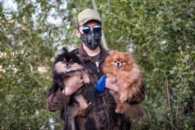 Solunum maskesi takan bir adam ormanda Pomeranya köpekleriyle yürüyor COVID-19 'dan korunuyor..