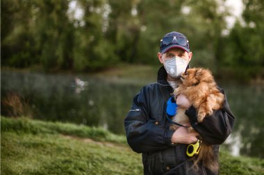 Solunum maskesi takan bir adam ormanda Pomeranya köpeğiyle yürüyor COVID-19 'dan korunuyor..