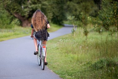 Yazın parkta bisiklet süren genç bir kadın..