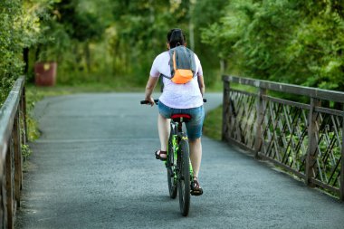 Yazın bir köprüde, parkta bisiklet süren bir kadın..