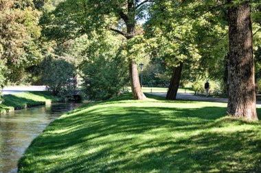Yazın güneşli bir günde yeşil bir parktan geçen nehir manzaralı İngiliz Parkı.