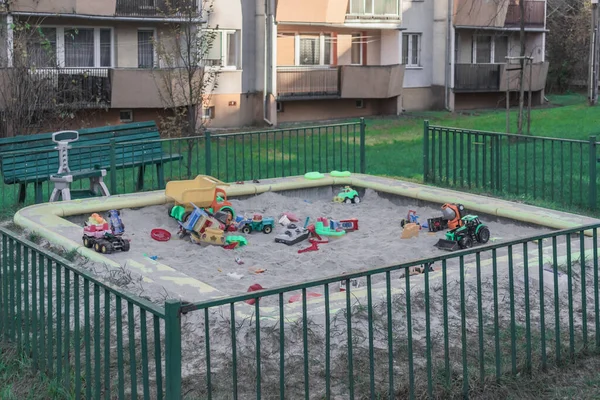 children's sandbox with scattered toys near a residential high-rise building
