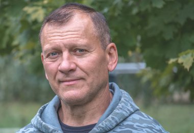 Yakışıklı orta yaşlı bir adamın portresi gülümseyerek sonbahar parkının arka planına bakıyor.