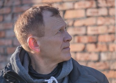 çekici orta yaşlı bir adam, 55-60 yaşlarında, tuğla bir duvara bakıyor, profil portresi