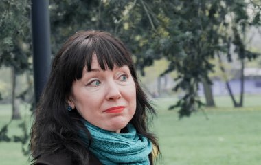 45 yaşında orta yaşlı esmer bir kadının portresi. Parkın arka planında duruyor.