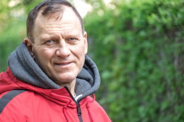 Orta yaşlı bir adam, 60 yaşında, tebessümle doğanın arka planında duruyor, bir adamın portresi..