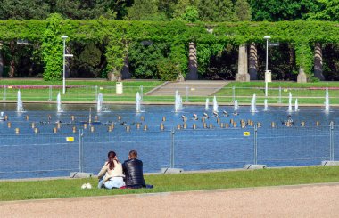Bir çift genç aşık, bir erkek ve bir kız göletin kenarında oturup çeşmeye bakıyorlar.