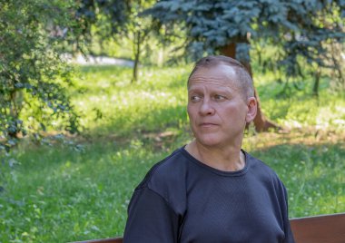 Siyah tişörtlü, çekici, yakışıklı, ciddi, olgun bir adamın portresi yeşil bir parkın arka planına bakıyor.