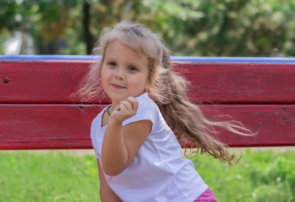 一个孩子的画像 一个快乐的小女孩 长发飘逸 坐在公园的长椅上 — 图库照片