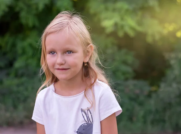 一个6岁至7岁的可爱可爱的金发碧眼的小女孩的画像 在一个阳光灿烂的绿色公园的背景下 带着微笑向前看 — 图库照片