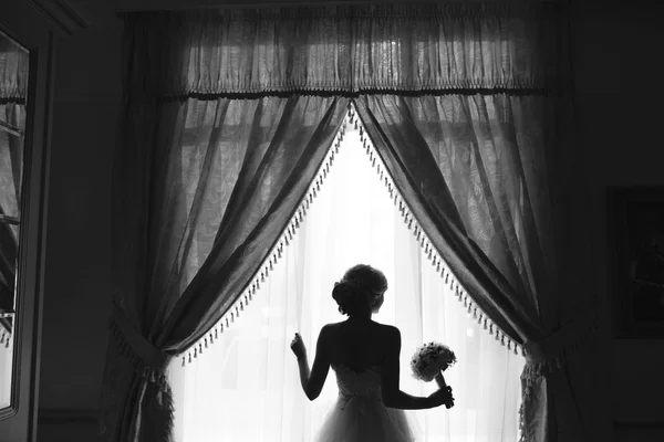 Beautiful bride in a wedding dress, by window. — Stock Photo, Image