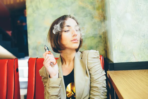 Menina senta-se e fuma cigarro eletrônico — Fotografia de Stock