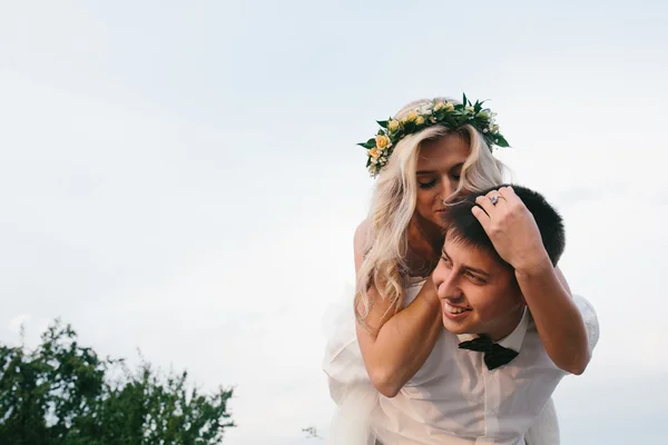 Bruidegom draagt bruid op zijn rug buitenshuis — Stockfoto