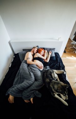 Hamile kadın, bir adam ve bir yatakta yatarken köpek