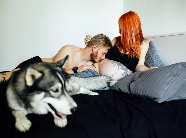 Donna incinta, uomo e cane sdraiati su un letto — Foto Stock