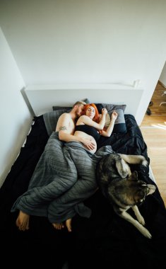 Hamile kadın, bir adam ve bir yatakta yatarken köpek
