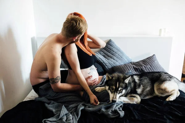 Donna incinta, uomo e cane seduti su un letto — Foto Stock