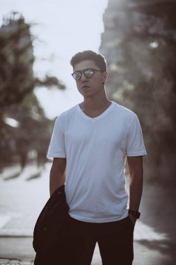 Adam şehrin caddesinde duruyor, kameralara ve çevresine bakıyor.