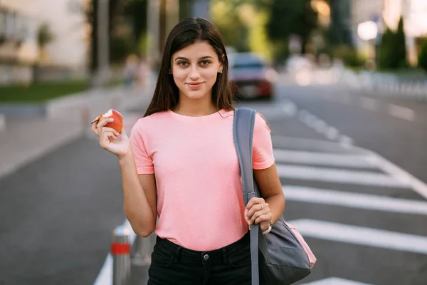 Ung kvinna som håller äpple mot en gata bakgrund — Stockfoto