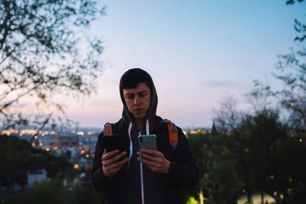 Молодий хлопець у парку фотографується на двох смартфонах — стокове фото