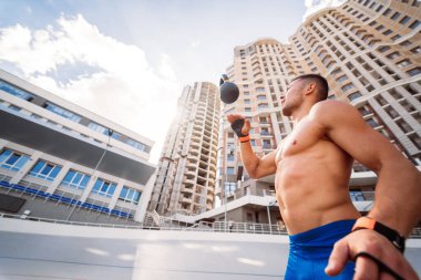 Yüksek bir binanın arka planında kettlebell ile antrenman yapan sporcu..
