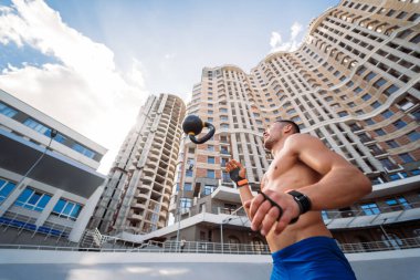 Yüksek bir binanın arka planında kettlebell ile antrenman yapan sporcu..