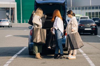 Alışveriş torbalarıyla arabada genç kadınlar var.