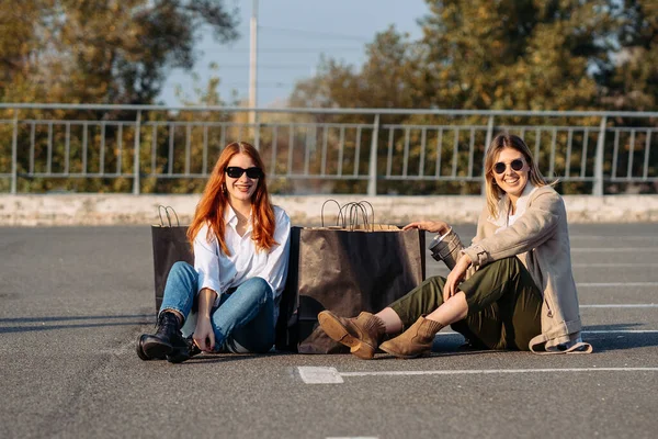 Mladé ženy s nákupními taškami sedí na parkovišti — Stock fotografie