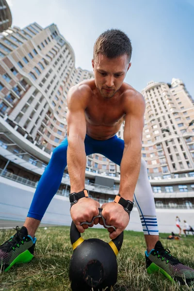 Sportive guy training with kettlebell on the background of a tall building. Stock Picture