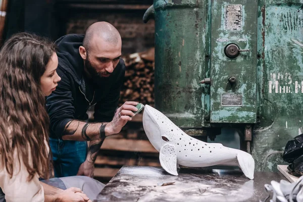 People carefully work on a ceramic whale in workshop