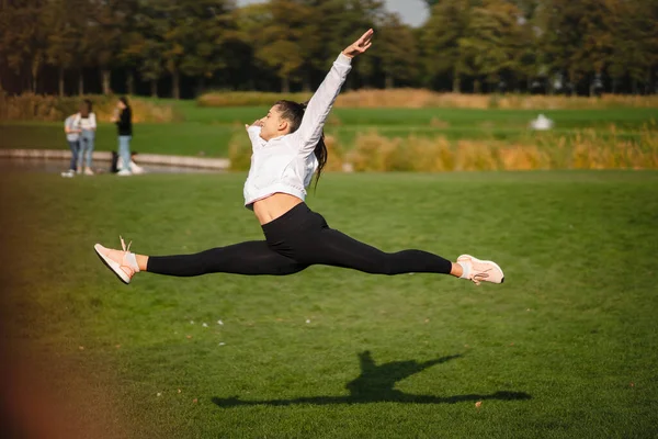 Спортивная девушка, прыгающая в воздух на природе, демонстрирует идеальное растяжение. — стоковое фото