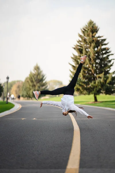 Женщина-спортсмен прыгает с сальто по дороге, делает упражнения на открытом воздухе. — стоковое фото