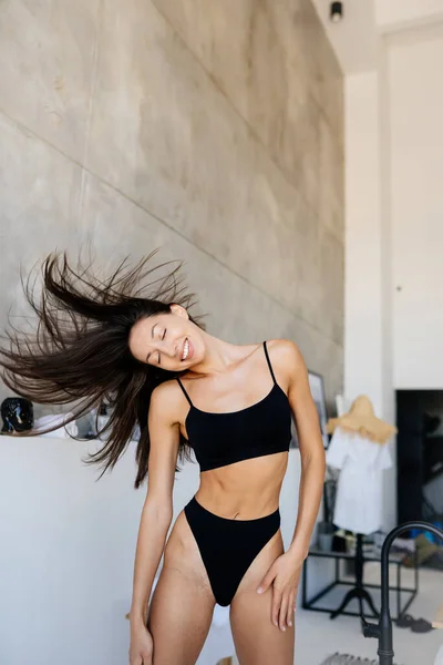 Jovem menina atraente em lingerie preta balançando a cabeça com o cabelo — Fotografia de Stock
