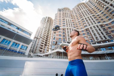 Yüksek bir binanın arka planında kettlebell ile antrenman yapan sporcu..