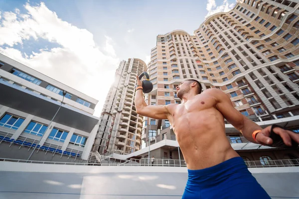 Sportive guy training with kettlebell on the background of a tall building. Stock Image