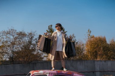 Genç bir kadın elinde çantalarla arabada duruyor.