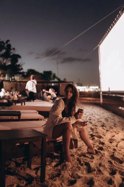 Jovem mulher está sentada na cadeira na praia da noite — Fotografia de Stock