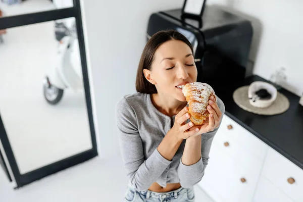 Портрет радісної жінки їсть смачний круасан вдома . — стокове фото