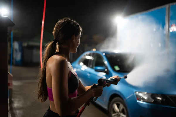 Araba yıkamada mavi araba yıkayan genç bir kadın. — Stok fotoğraf