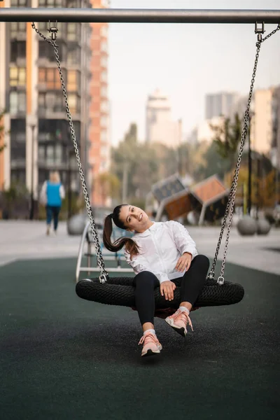 Jeune femme monte sur une balançoire à l'aire de jeux. — Photo
