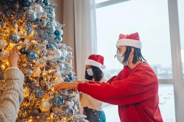 Seorang pemuda menghias pohon Natal dengan masker medis. — Stok Foto