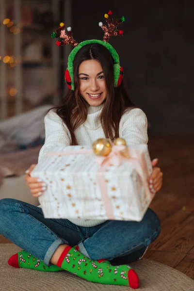 Gadis dengan hadiah tersenyum ke kamera. Dia memakai tanduk Natal.. — Stok Foto