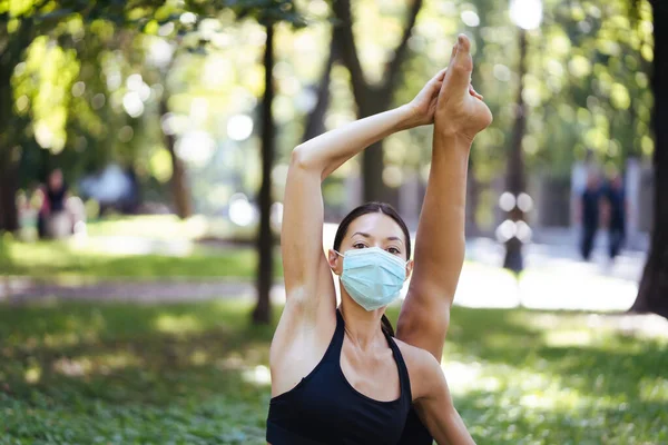 Jeune femme sportive dans un masque de protection médicale, faire du yoga dans le parc — Photo