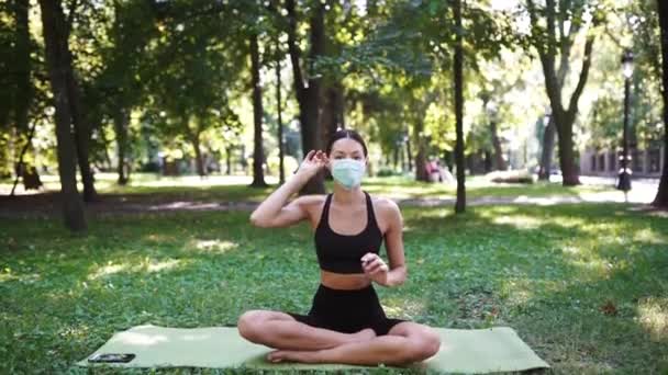 Атлетичная молодая женщина в медицинской защитной маске, занимающаяся йогой в парке — стоковое видео